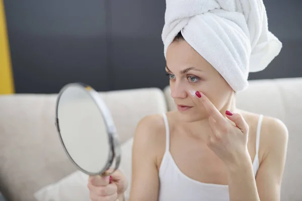 Mladá žena drží zrcadlo v rukou a nanášení krému na její obličej v koupelně — Stock fotografie