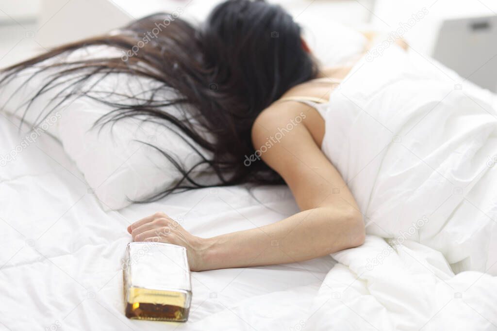 Women lying in white bed with bottle of whiskey in hand