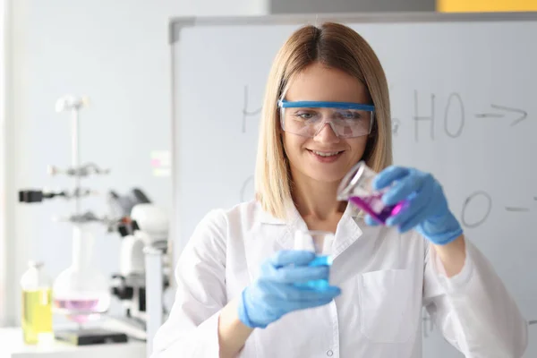Žena chemik v ochranných brýlích nalévání kapaliny z baňky — Stock fotografie