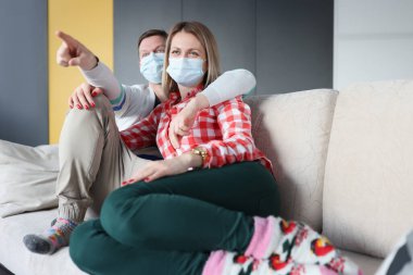 Karı koca koruyucu sağlık maskeleriyle kanepede oturuyorlar.