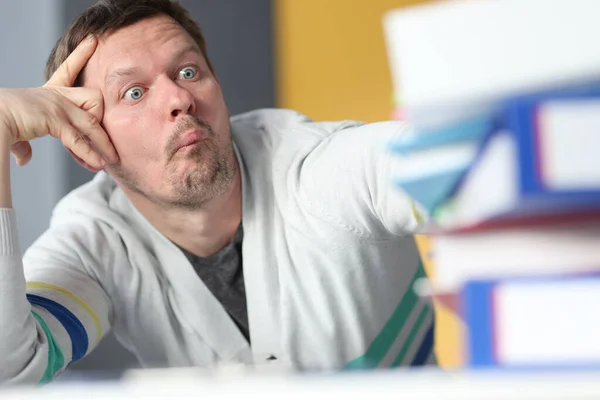 Uomo stanco seduto a tavola con molte cartelle di carta — Foto Stock