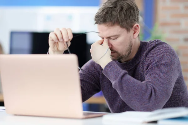 Tired man siting in front of laptop screen and holding glasses in hands — Stock Photo, Image