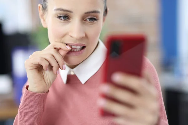 Junge Frau beißt sich auf Fingernägel und schaut auf Telefonbildschirm — Stockfoto