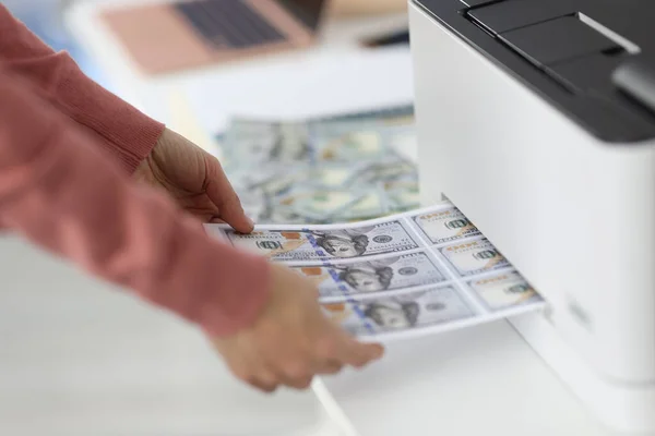 Female hands pulling out paper with printed dollar bills from printer