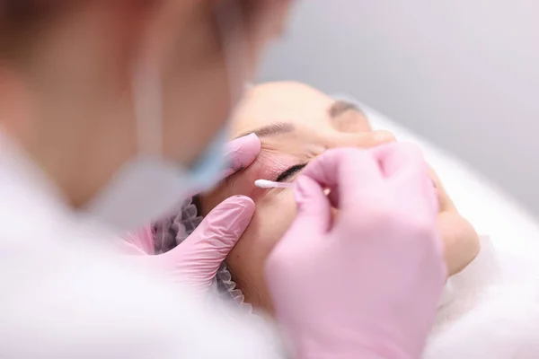 Beautician vegen crème op klanten ooglid met wattenstaafje closeup — Stockfoto