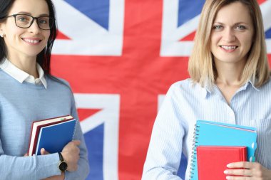 Two smiling women stand with notebooks in front of British flag clipart