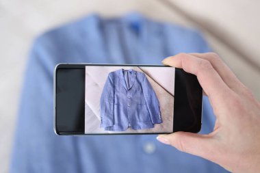 Kameralı telefonda mavi ceketin fotoğrafını çeken kadın.