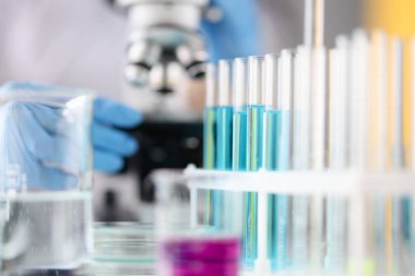 Mikroskobun arka planında duran mavi sıvılı test tüpleri