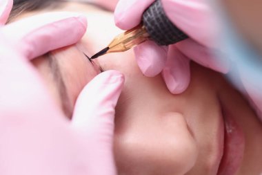 Eldivenli bir güzellik uzmanı müşterilerin göz kapaklarına siyah mürekkep sürüyor.