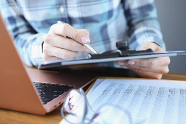 Müdür masasında oturuyor ve elinde kalemle belgeleri tutuyor.