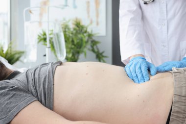 Doktor hastaların karnını kanepede yakından muayene ediyor.
