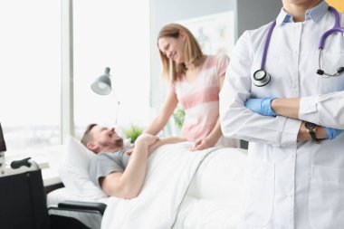 Mutlu adam hastane yatağında yatıyor. Elini doktorun yanındaki kadın tutuyor.