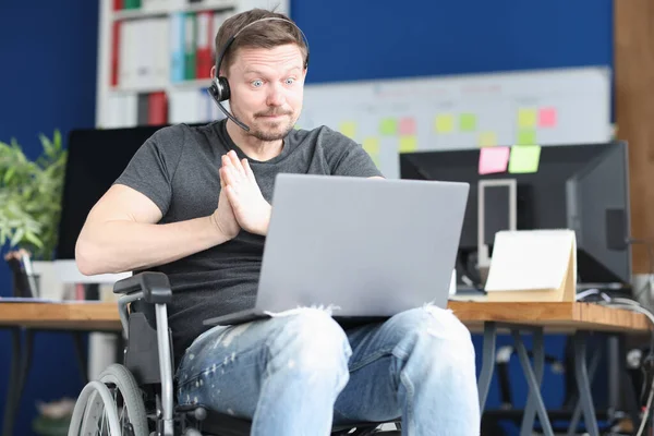 Hombre en silla de ruedas y con auriculares con micrófono funciona en el ordenador portátil —  Fotos de Stock