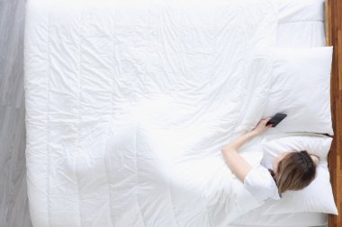 Young woman lying in bed with mobile phone top view