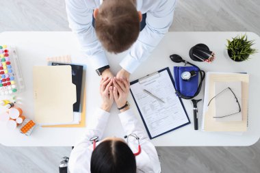 Doctor holding patients hands in clinic top view