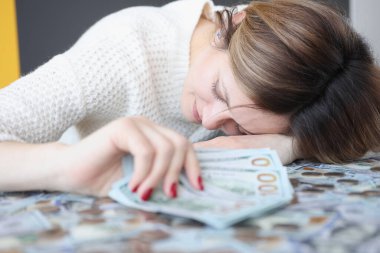Young woman lying on pile of money and holding dollars in her hands