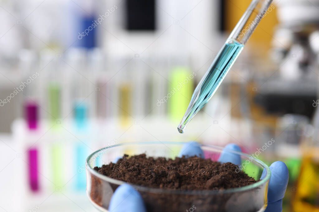 Liquid is dropped from glass pipette into flask with soil