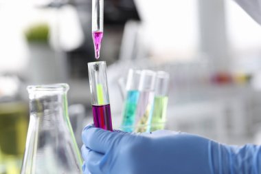 Bilim adamı pembe sıvıyı pipetle test tüpünün içine atıyor.