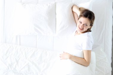 Genç kadın yatakta uzanıyor ve gülümsüyor.