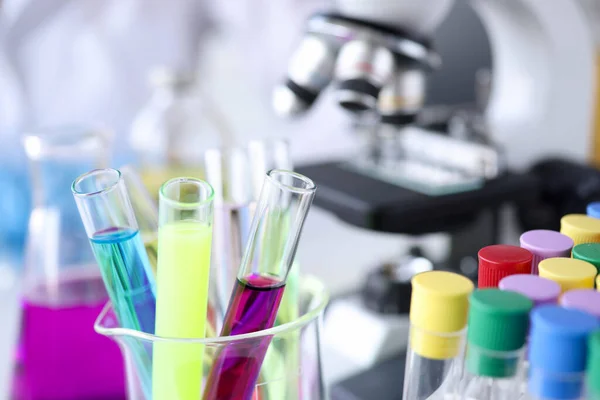 Chemical test tubes with multi-colored liquids on background of microscope