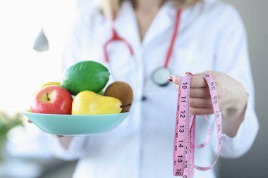 Beslenme uzmanının elinde bir tabak meyve ve santimetre var.