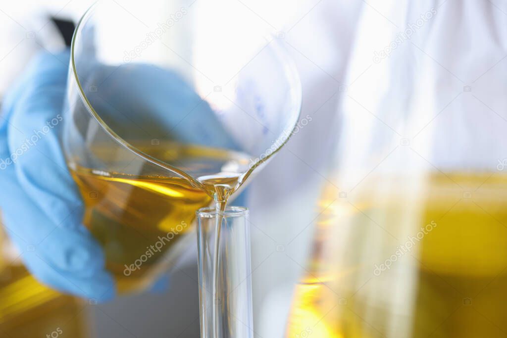 Scientist pours clear golden liquid into glass flask