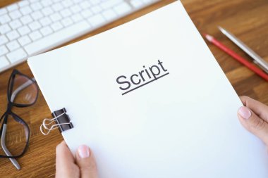 Kadın eller senaryoyu yakın plan masa üzerinde tutuyor.
