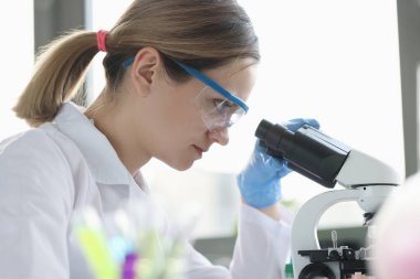 Woman scientist with glasses conducts research through microscope