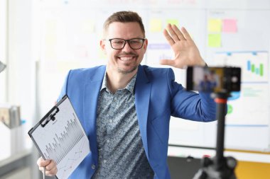 Smiling businessman holds financial clipboard in his hands and records video on camera
