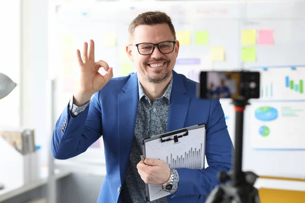 Young business coach showing ok gesture in front of mobile phone camera