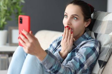 Şaşırmış bir kadın koltukta otururken akıllı telefon ekranına bakar.