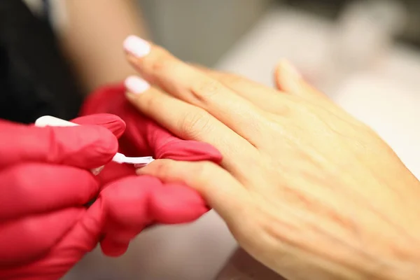 Close-up of manicurist covering nails of client with light nail polish