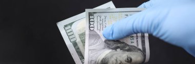 Eldivenli el 100 dolarlık banknot tutuyor.