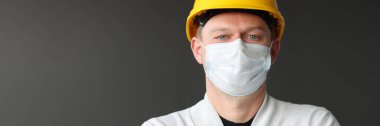 Sarı kast ve tıbbi koruyucu maskeli erkek inşaat işçisi..