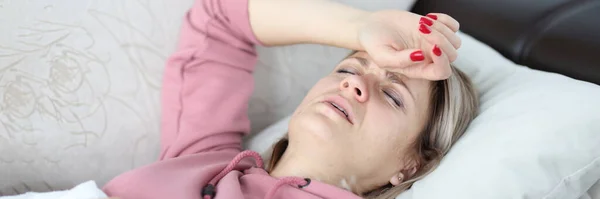 Mujer cansada yace en el sofá con los ojos cerrados y sostiene su mano en la frente. — Foto de Stock