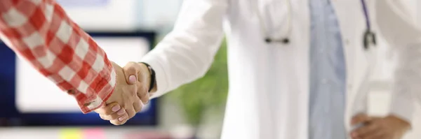 Arts met stethoscoop rond de nek schudden patiënten hand in hand kliniek closeup — Stockfoto