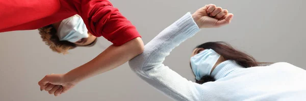 Дві жінки в захисних медичних масках торкаються один одного ліктями — стокове фото