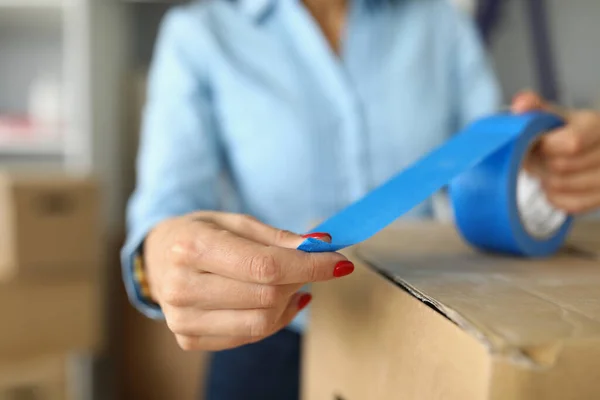 Close-up of female packs up things in carton boxes with blue scotch — Stock Photo, Image