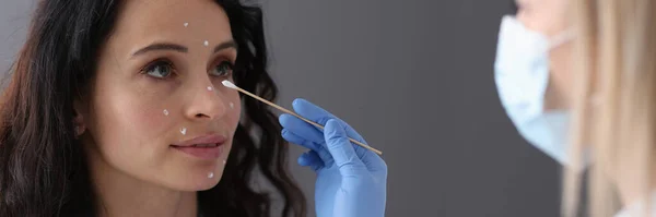Schoonheidsspecialiste brengt witte crème aan op het gezicht van patiënten met wattenstaafje — Stockfoto