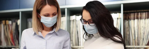Deux femmes portant des masques médicaux protecteurs sélectionnant le tissu du catalogue — Photo