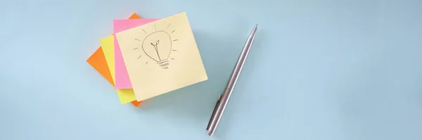 La bombilla está dibujando en un pedazo de papel. Muchas pegatinas de colores y bolígrafo acostado en la mesa —  Fotos de Stock