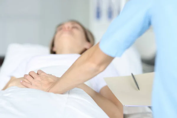 Dokter houdt liggend patiënt met de hand op ziekenhuisbed. — Stockfoto