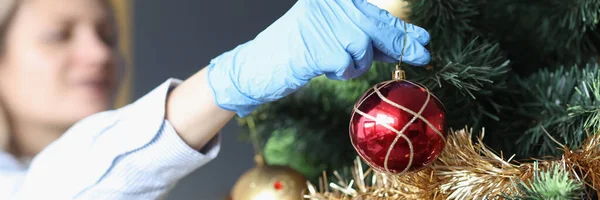 Frau in schützenden Gummihandschuhen hängt Ball in Großaufnahme am Weihnachtsbaum — Stockfoto