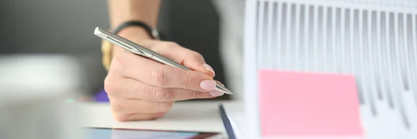 Frau schreibt mit Kugelschreiber in Dokumente mit Diagrammen und Diagrammen am Tisch in Großaufnahme — Stockfoto