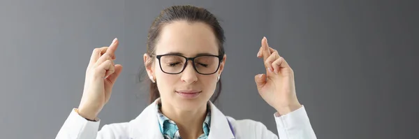 Vrouwelijke arts met gesloten ogen houdt gekruiste vingers — Stockfoto