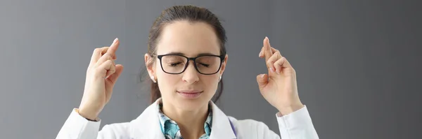 Médica com olhos fechados segura dedos cruzados — Fotografia de Stock