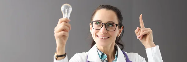 Sorrindo médico fêmea segurando lâmpada e polegar para cima — Fotografia de Stock