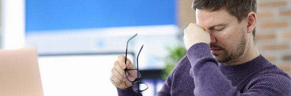 Man siting at table in office and holding bridge of his nose
