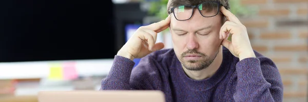 Egy férfi ül a laptop előtt és fogja a fejét. — Stock Fotó
