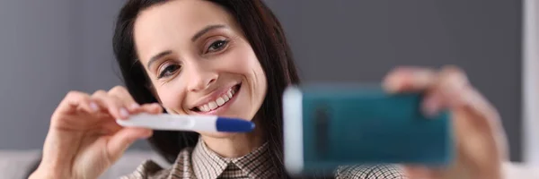 Smiling woman shows pregnancy test in smartphone — Stock Photo, Image